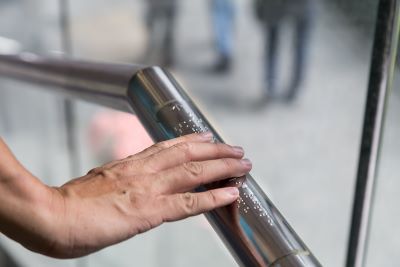 Hand touching handrail with Braille.
